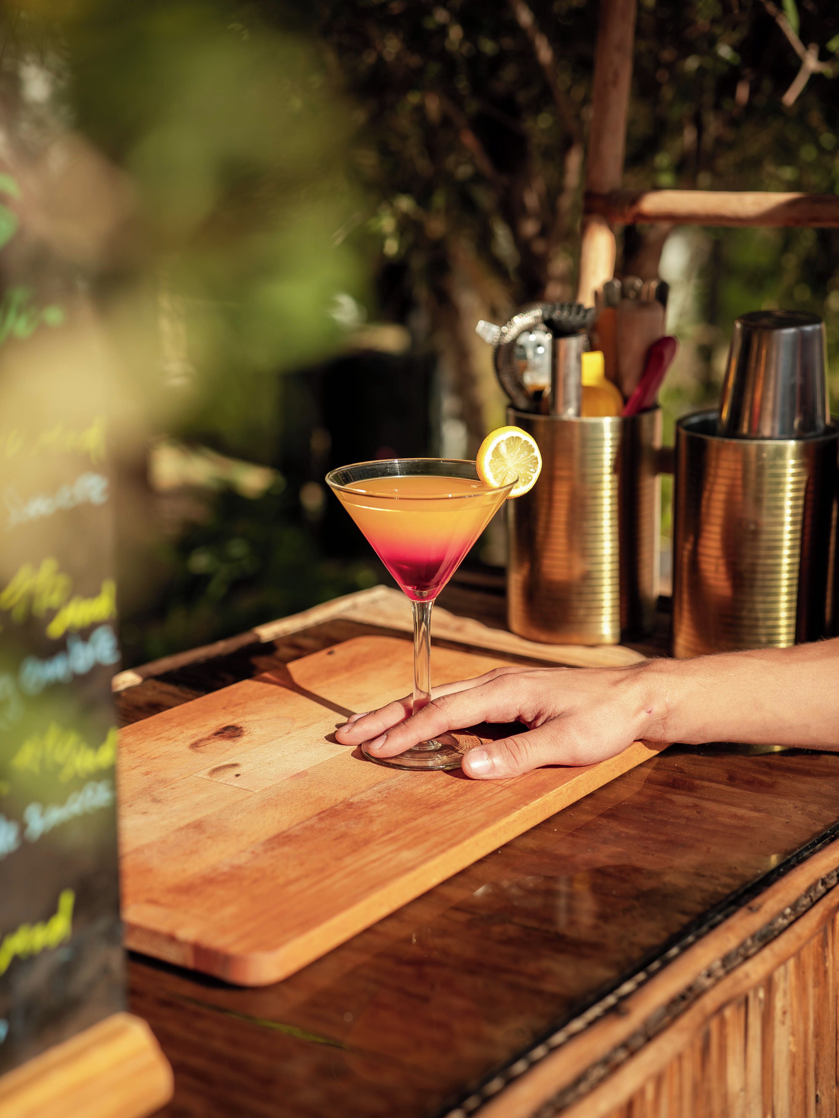 A hand holding a cocktail glass on a wooden bar counter.