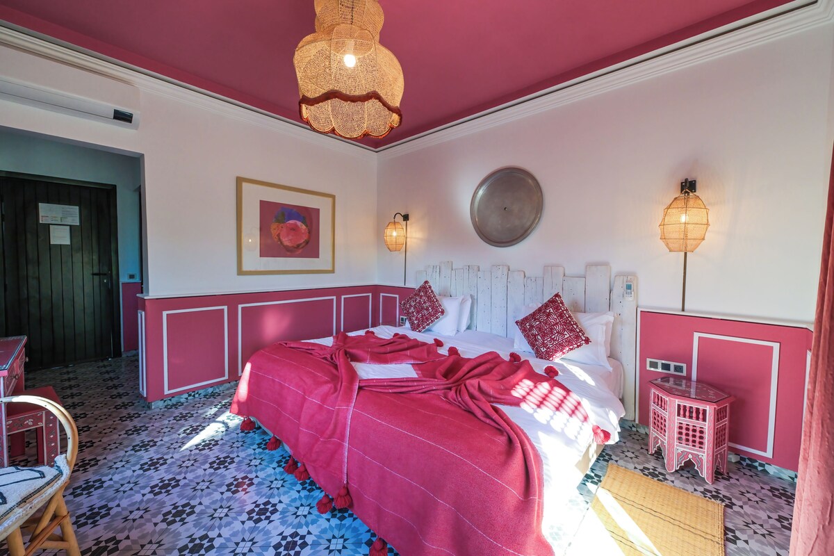 A bedroom with a large bed, a small stool, and a door.