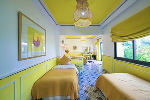 A room with two beds, a window with a view, a chandelier, and a mirror on the wall. - Maison Daouia (Marrakech)