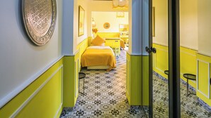 A hallway with a geometric patterned floor, a bed with yellow bedding, and a decorative wall plate. - Maison Daouia (Marrakech)