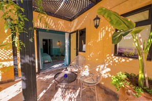 A patio with a table and chairs, a potted plant, and a view of the interior. - Maison Daouia (Marrakech)