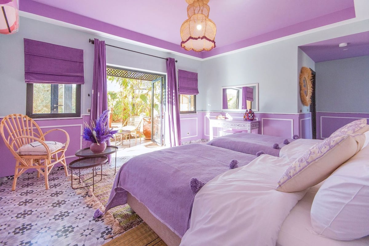 A bedroom with two beds, a chair, a vanity, and a window with curtains.