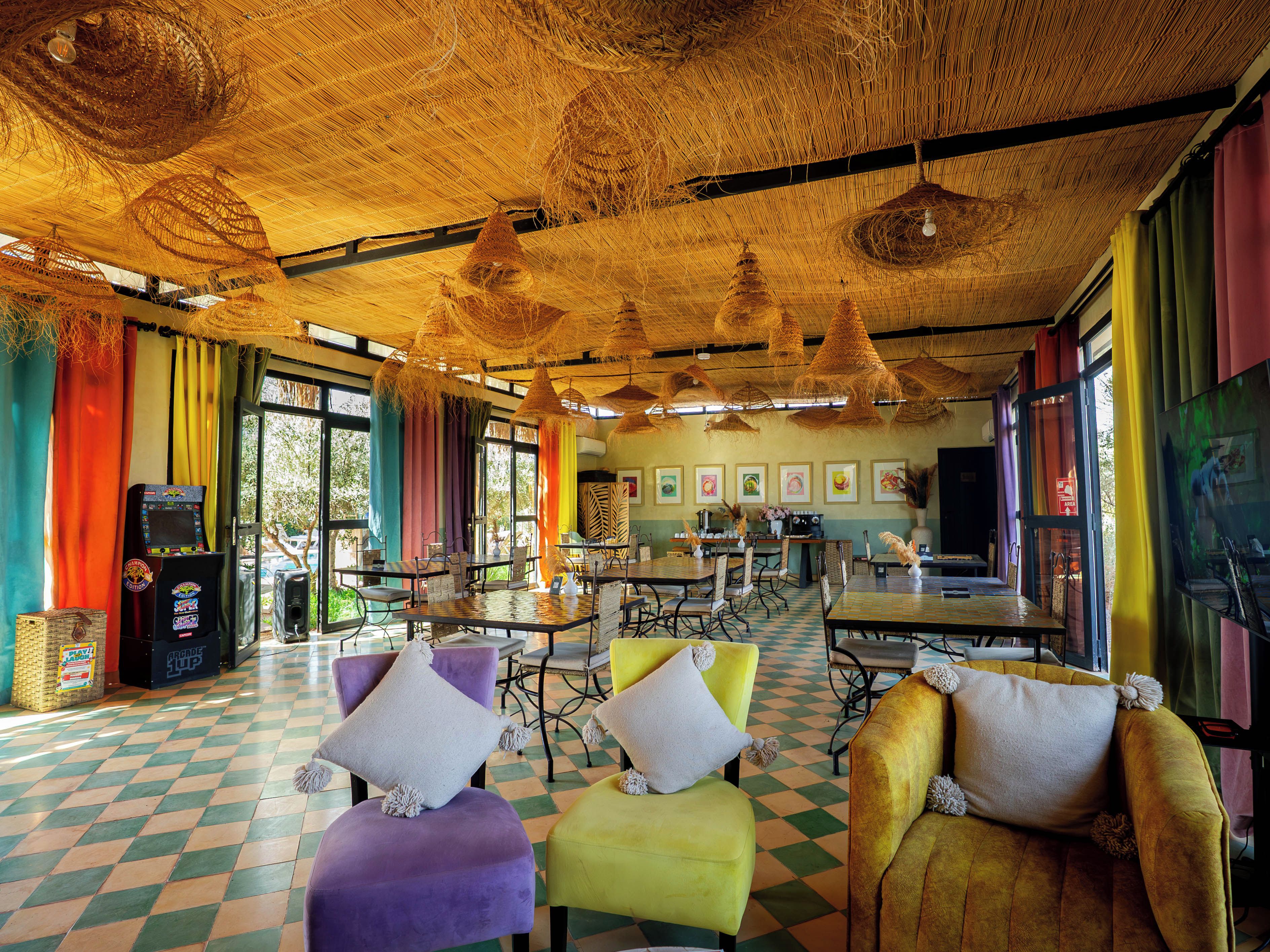 A spacious dining area with checkered flooring, colorful chairs, and a thatched ceiling.