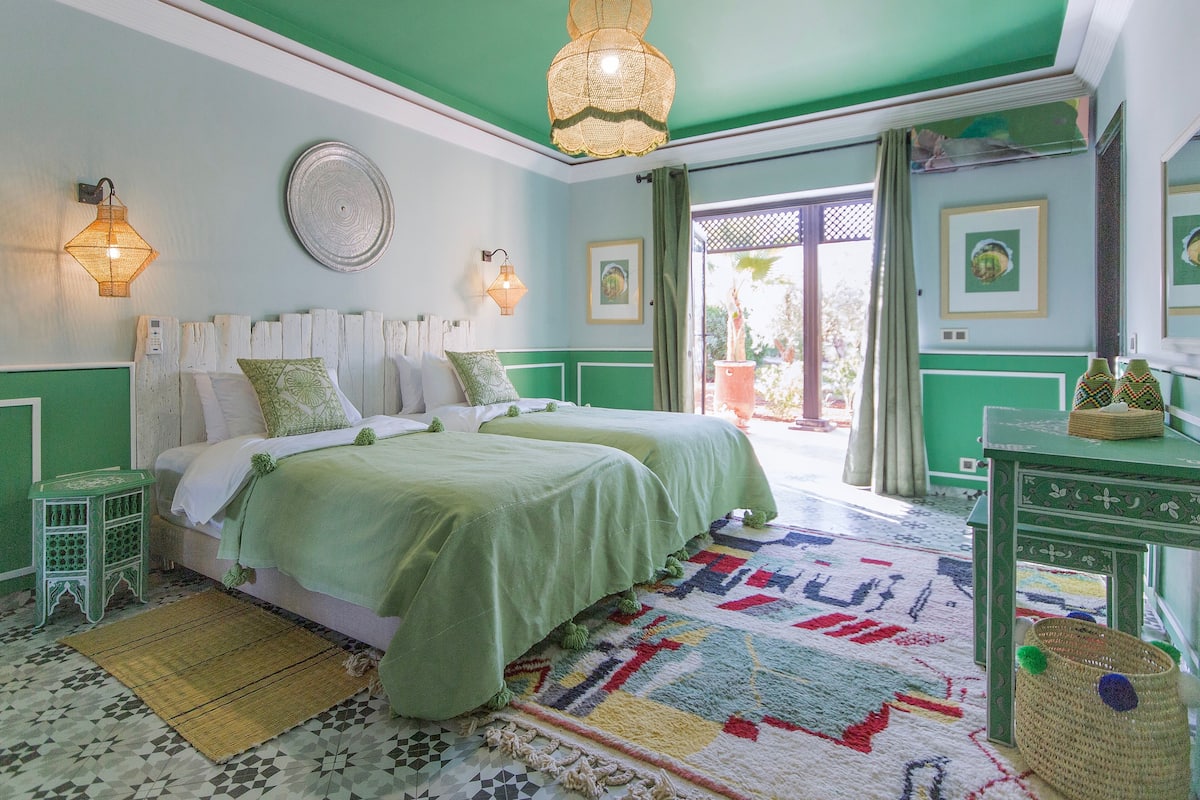 A room with two beds, a green and white color scheme, a patterned rug, and a view through a door.