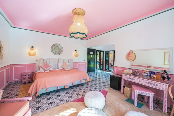A bedroom with a pink ceiling, a bed with a pink headboard, a desk with a mirror, and a patterned floor.