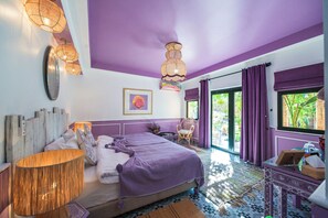 A bedroom with a bed, bedside table, lamp, and a view of the outdoors.