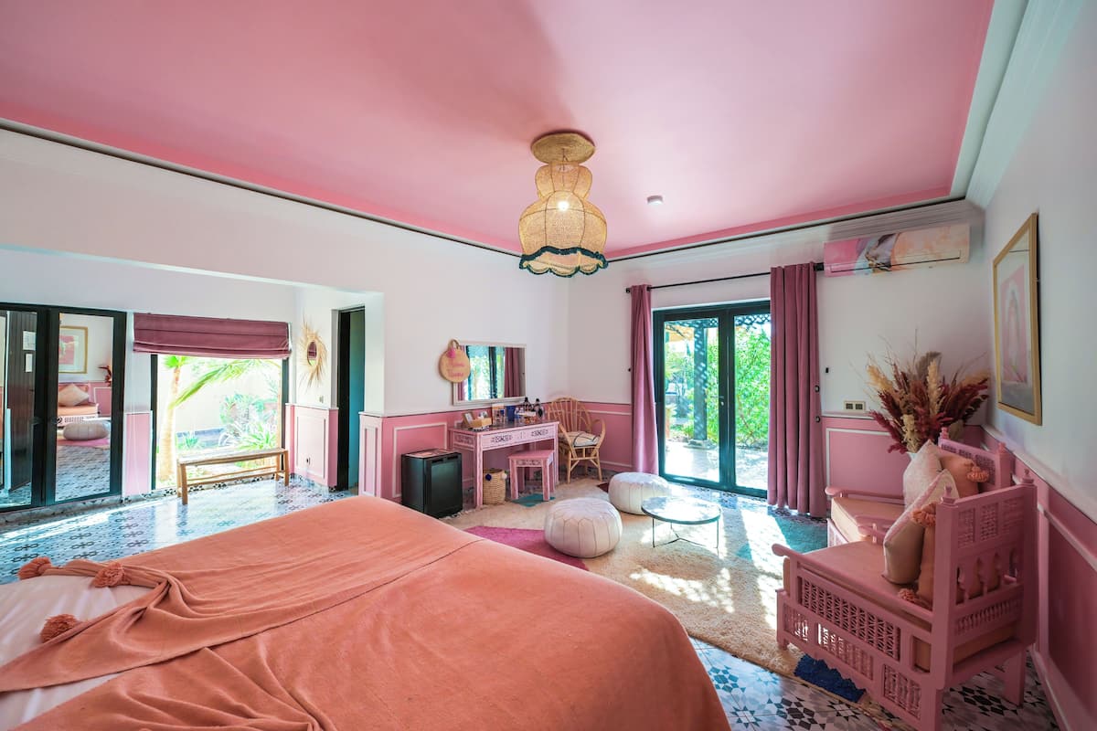 A pink-themed bedroom with a bed, desk, and chair, and a view of the outdoors.