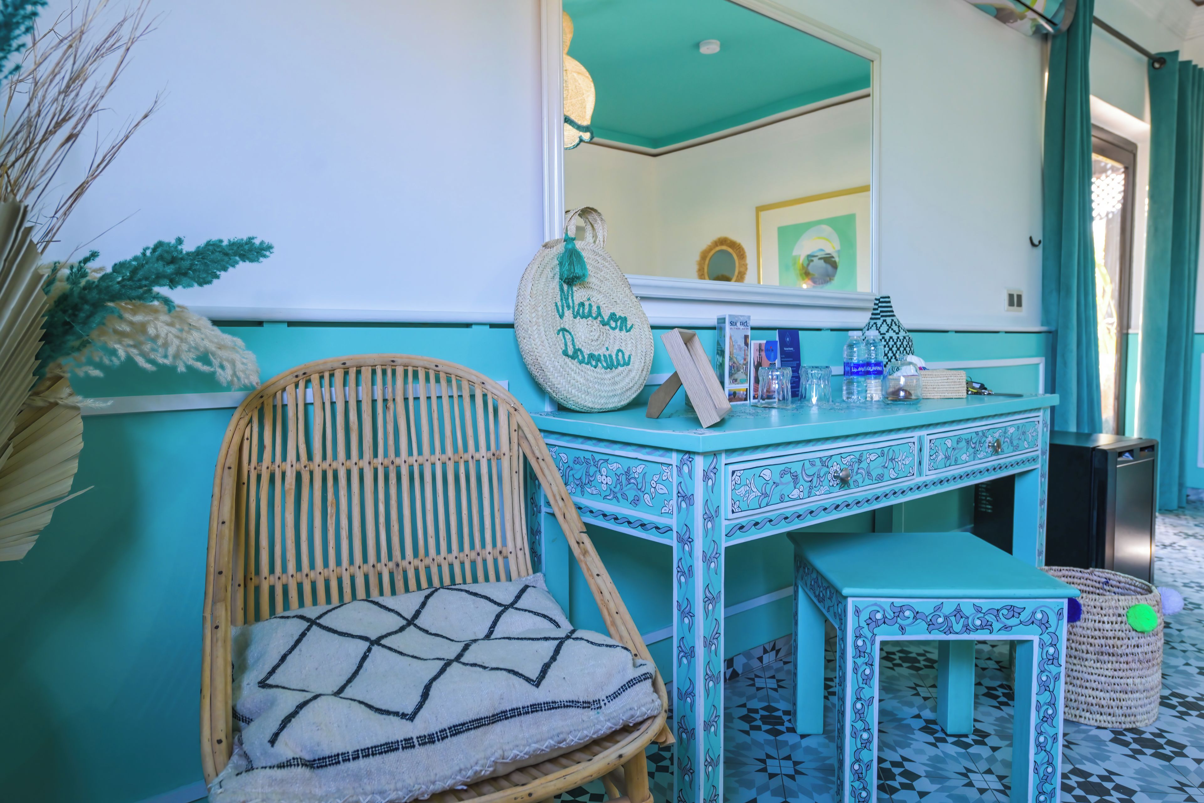 Een badkamer met een blauwgroene wastafel, een rieten stoel en een kleine tafel.