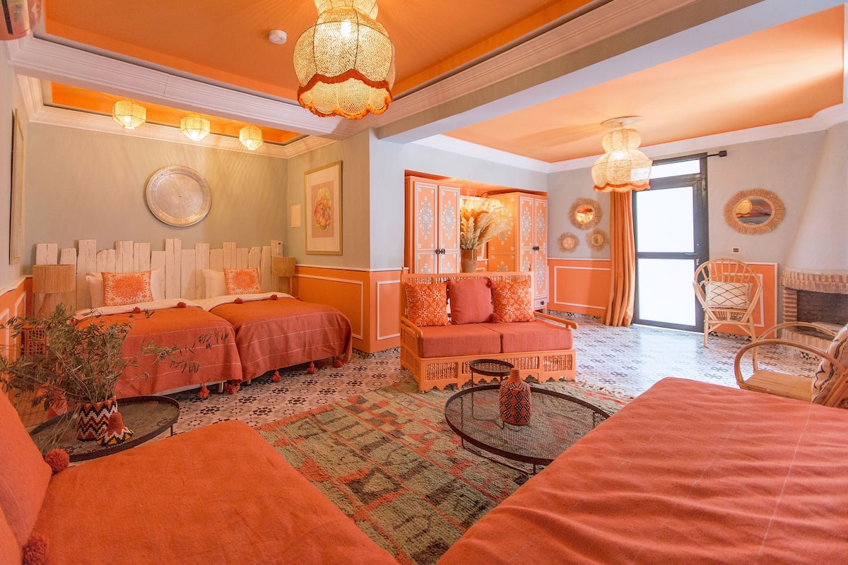 A room with two beds, a sofa, a small table, and a chair. There are decorative pillows and a vase on the sofa.