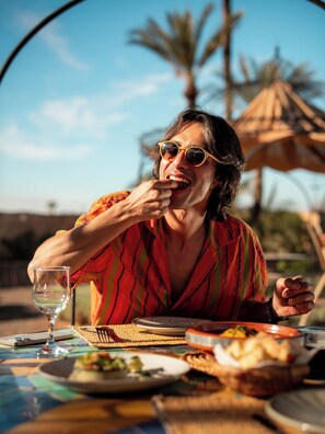 A person dining outdoors with a table set for a meal, a glass of water, and a basket of food. - Maison Daouia (Marrakech)