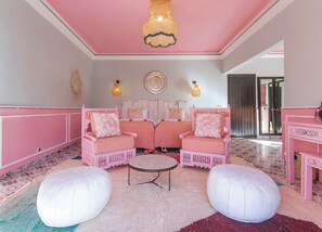 A room with two pink armchairs, a round coffee table, and a white ottoman.