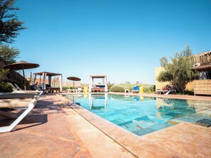 A swimming pool with lounge chairs and umbrellas, surrounded by vegetation and a clear sky. - Maison Daouia (Marrakech)