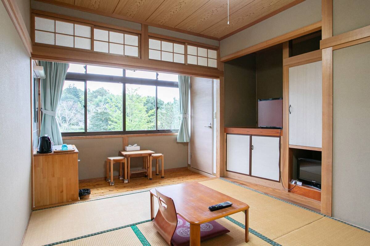 Ein traditioneller japanischer Raum mit Tatami-Bodenbelag, einem niedrigen Tisch mit Kissen, einem Fernseher und einem Schrank.