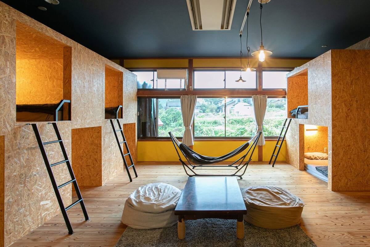 Ein Zimmer mit einer Hängematte, einer Leiter, einem Bett und Blick auf grüne Vegetation.
