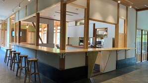 A bar area with stools, a counter, and a kitchen in the background. - MIZUKAMISO (Mizukami)