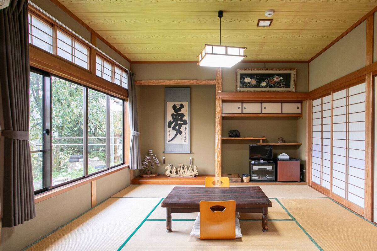 Ein traditioneller japanischer Raum mit Tatami-Boden, einem niedrigen Tisch, Schiebetüren und einem hängenden Kunstwerk.