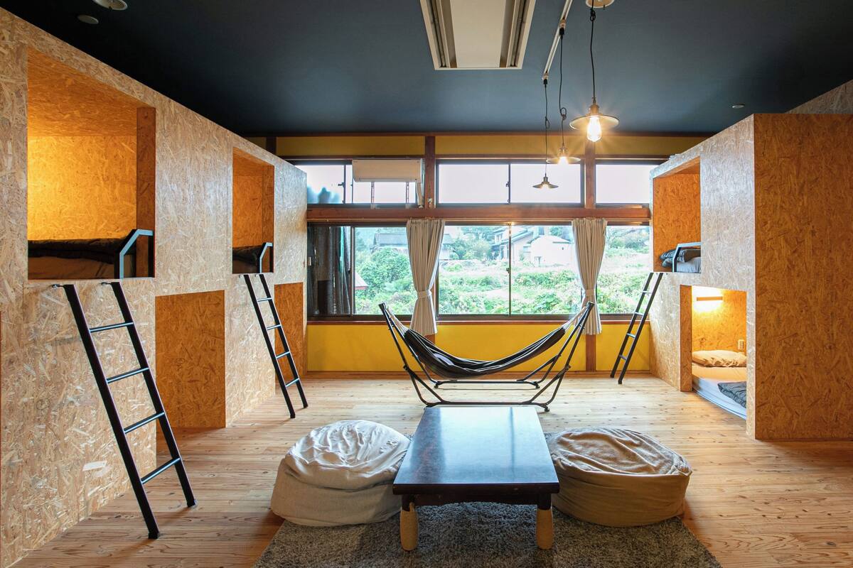 Ein Zimmer mit einer Hängematte, Sitzsäcken, einer Leiter und Blick durch große Fenster.