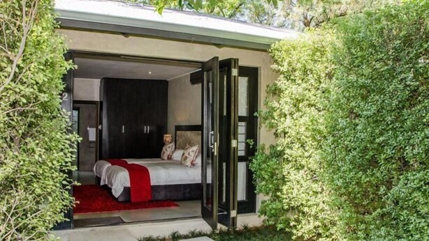 A modern bedroom with a large bed, a walk-in closet, and a glass door leading to a garden. - 9 On Kromellenboog Guesthouse (Metsimaholo)