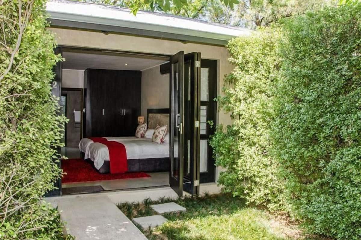 A modern bedroom with a large bed, a walk-in closet, and a glass door leading to a garden.