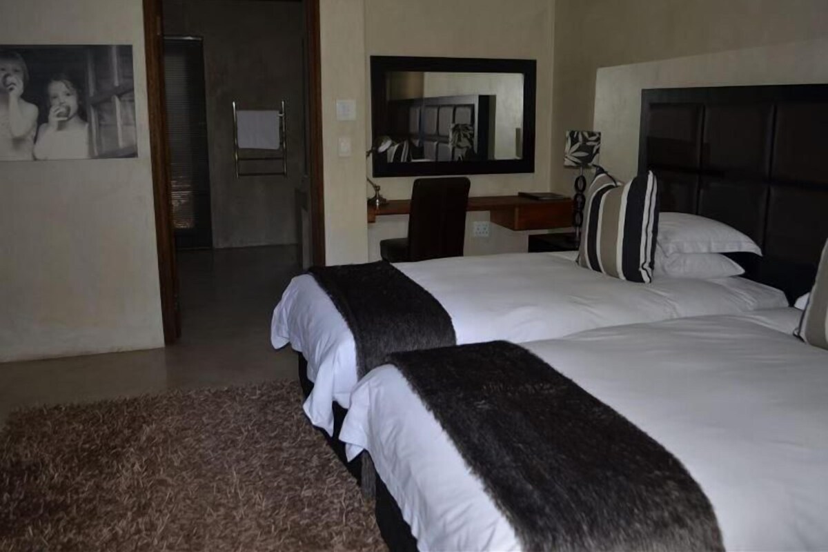 Ein Hotelzimmer mit zwei Betten, einem Schreibtisch, einem Stuhl, einem Spiegel und einer Tür zu einem weiteren Raum.
