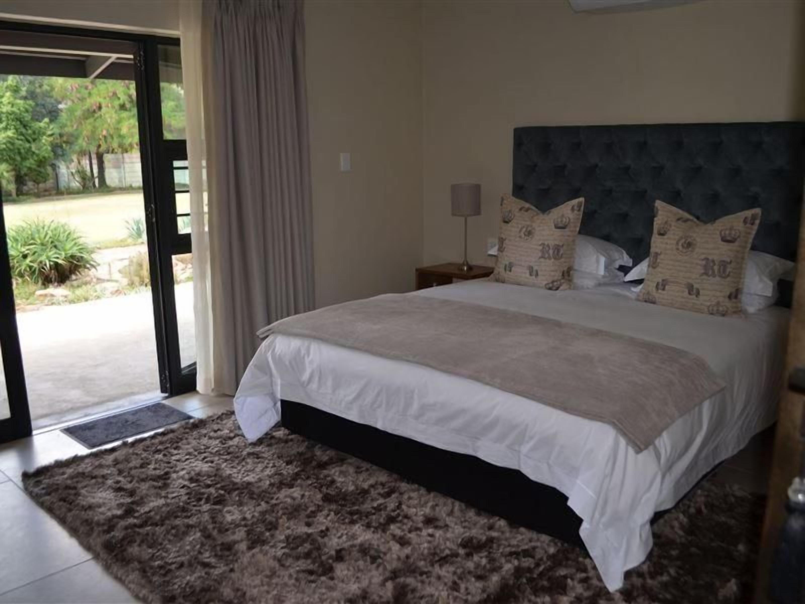A bedroom with a large bed, a headboard, a nightstand, and a view through a glass door.
