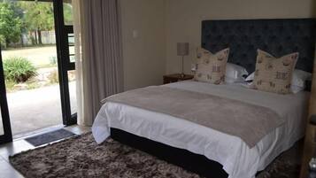 A bedroom with a large bed, a headboard, a nightstand, and a view through a glass door.