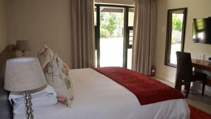 Une chambre d’hôtel avec un lit, un bureau, une chaise, une lampe et un téléviseur.