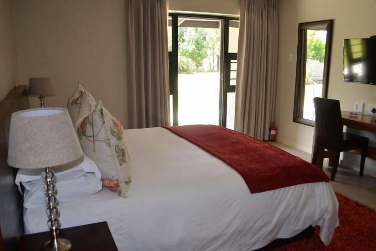 Une chambre d’hôtel avec un lit, un bureau, une chaise, une lampe et un téléviseur.