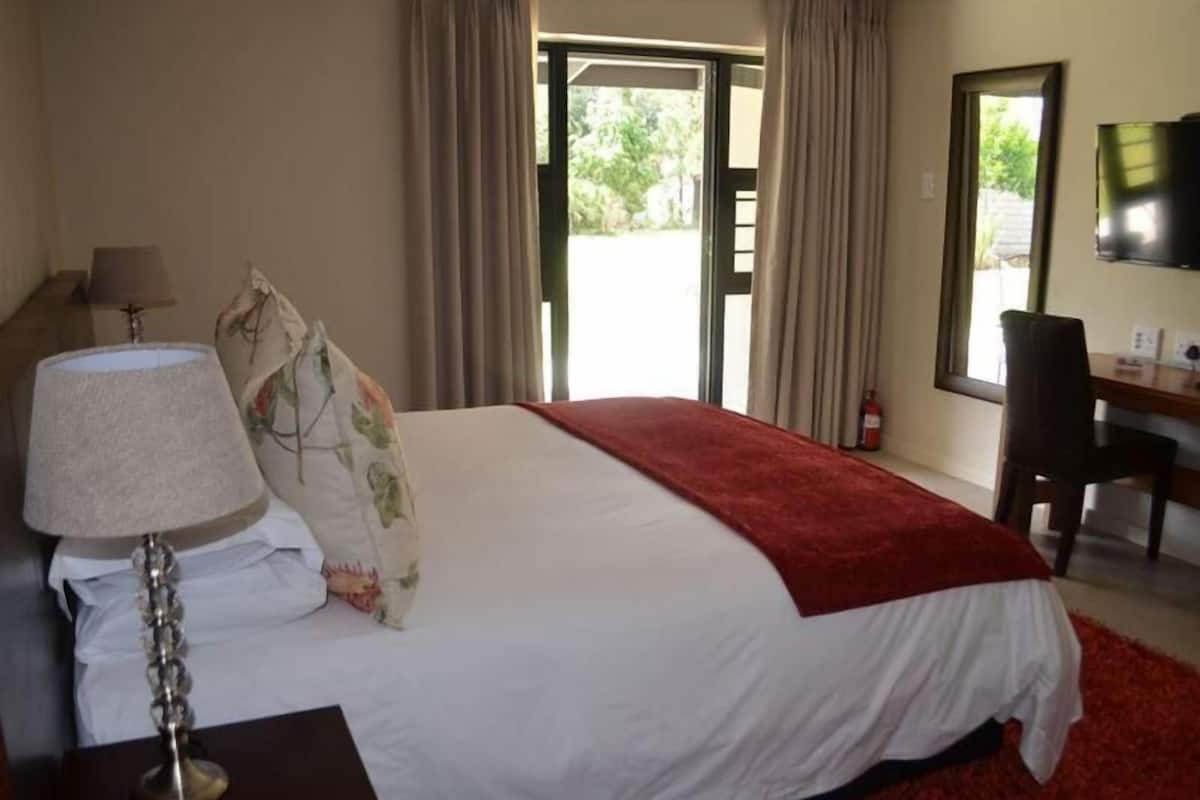 A hotel room with a bed, a desk, a chair, a lamp, and a TV.