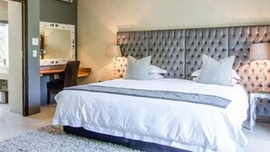 Une chambre à coucher avec un grand lit, une tête de lit capitonnée, une table de chevet avec des lampes et un miroir au mur.