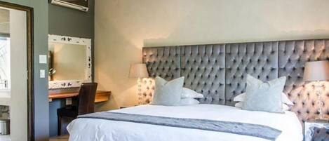 Un dormitorio con una cama grande, cabecera, mesitas de noche, un espejo y un escritorio.