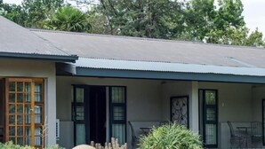A house with a covered porch, a garden with various plants and flowers, and a large rock in the center. - 9 On Kromellenboog Guesthouse (Metsimaholo)