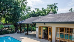 A poolside area with a pool, a covered seating area, and a building with large windows. - 9 On Kromellenboog Guesthouse (Metsimaholo)