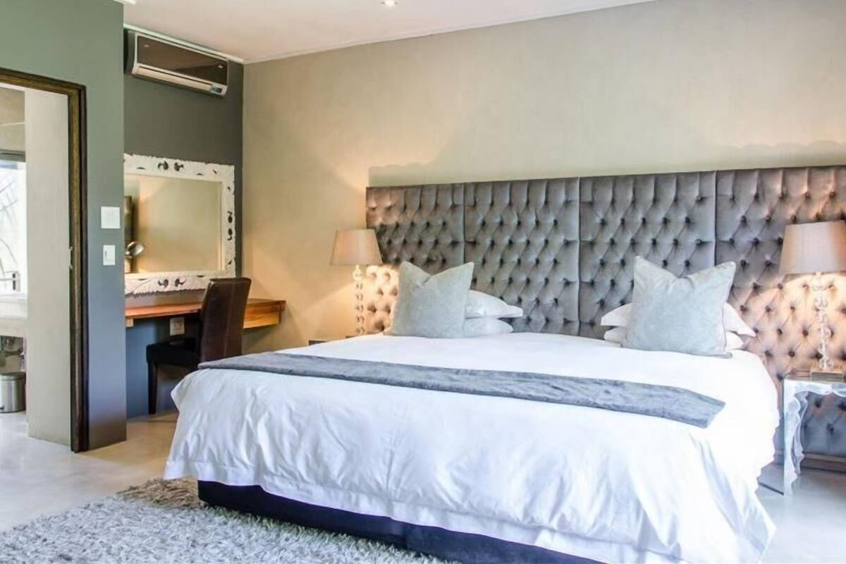 Une chambre à coucher avec un grand lit, une tête de lit capitonnée, une table de chevet avec des lampes et un miroir au mur.