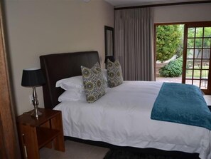 A bedroom with a large bed, two pillows, a bedside table with a lamp, and a view of greenery through a window. - 9 On Kromellenboog Guesthouse (Metsimaholo)