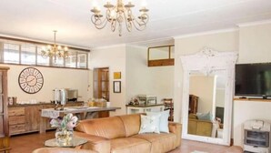 A living room with a leather sofa, a coffee table, a chandelier, and a large mirror. - 9 On Kromellenboog Guesthouse (Metsimaholo)