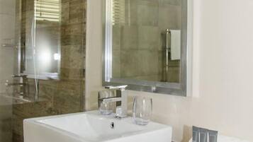 Un baño moderno con un lavamanos grande de color blanco, dos vasos de vidrio, un espejo y un toallero con artículos de aseo.