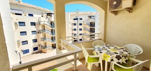 A balcony with a table and chairs, overlooking a building with multiple balconies and windows.