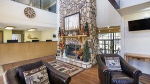 Eine Lobby mit Kamin aus Stein, Ledersofas mit gemusterten Kissen, einer Wanduhr und einem Empfangsschalter.