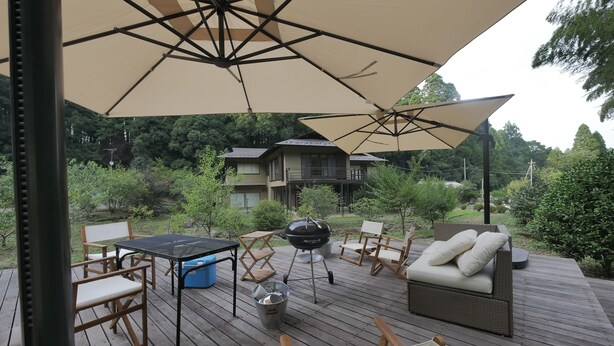 En træterrasse med udendørs møbler, grill og en stor parasol, der giver skygge.