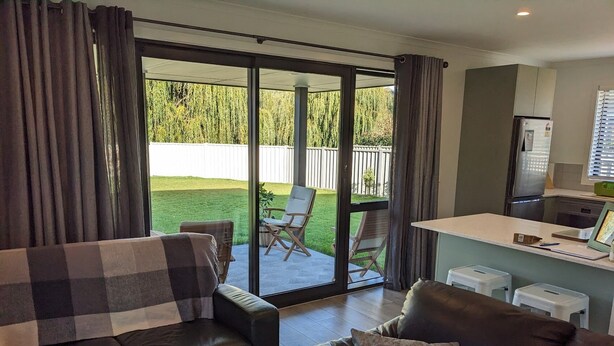 Ein Wohnzimmer mit einer Couch, einem Couchtisch und einem Essbereich mit einer Küchenzeile. Eine Glastür öffnet sich zu einer Terrasse mit Sitzgelegenheiten.