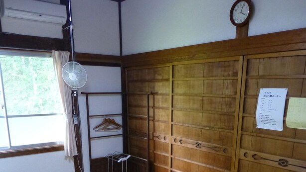 Une pièce de style japonais traditionnel, avec un sol recouvert de tatamis, une armoire en bois, un éventail et une horloge au mur.