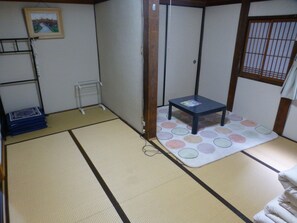 A tatami mat room with a small table, a shelf, and a picture on the wall. - Omihachiman Youth Hostel (Omihachiman)