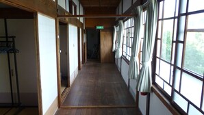 Un couloir doté d’un plancher en bois, de grandes fenêtres avec des rideaux et de portes coulissantes traditionnelles japonaises.