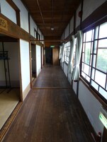Un pasillo con piso de madera, ventanas grandes con cortinas y puertas correderas tradicionales japonesas.
