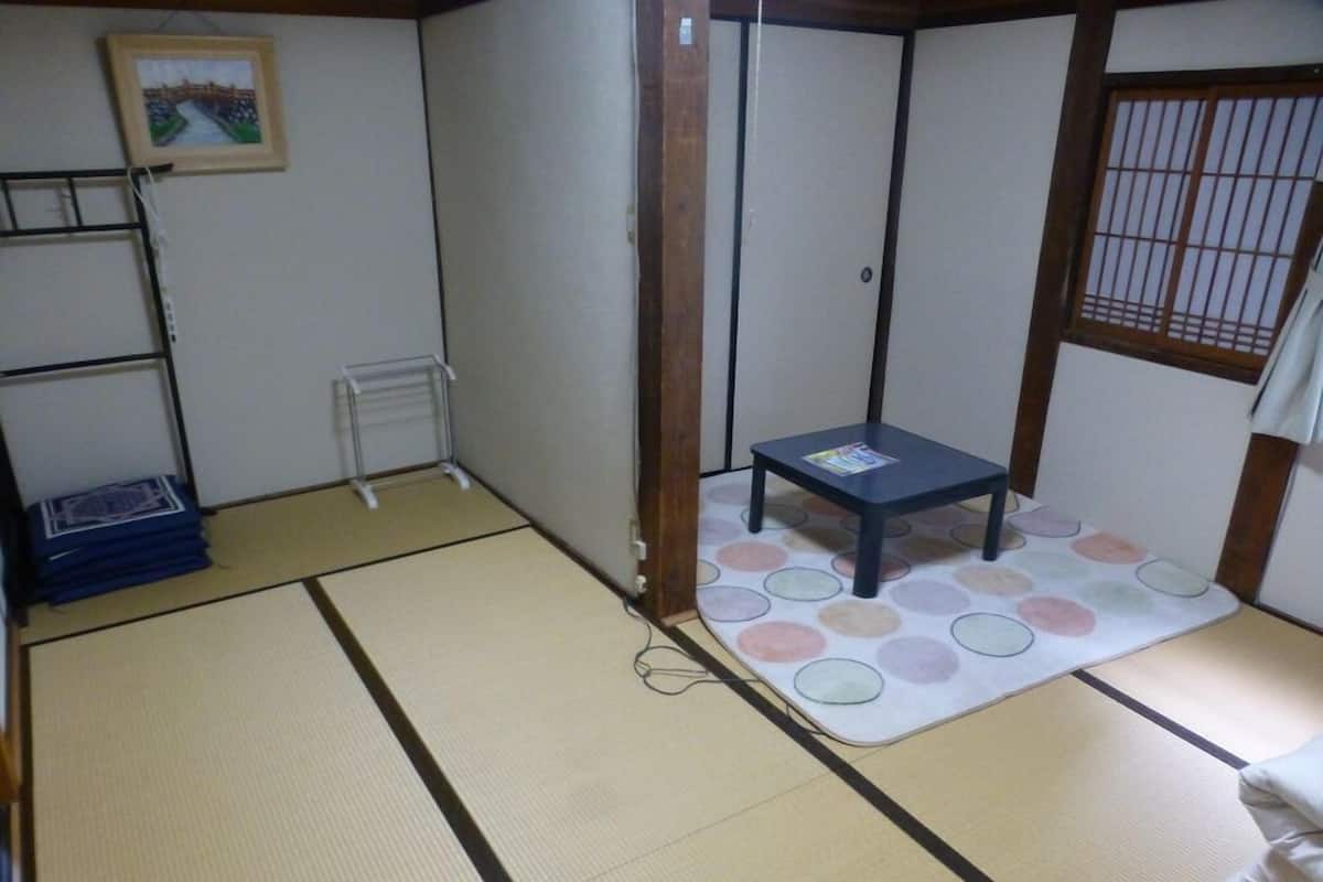 Ein Raum mit Tatami-Matten, einem kleinen Tisch, einem Regal und einem Bild an der Wand.
