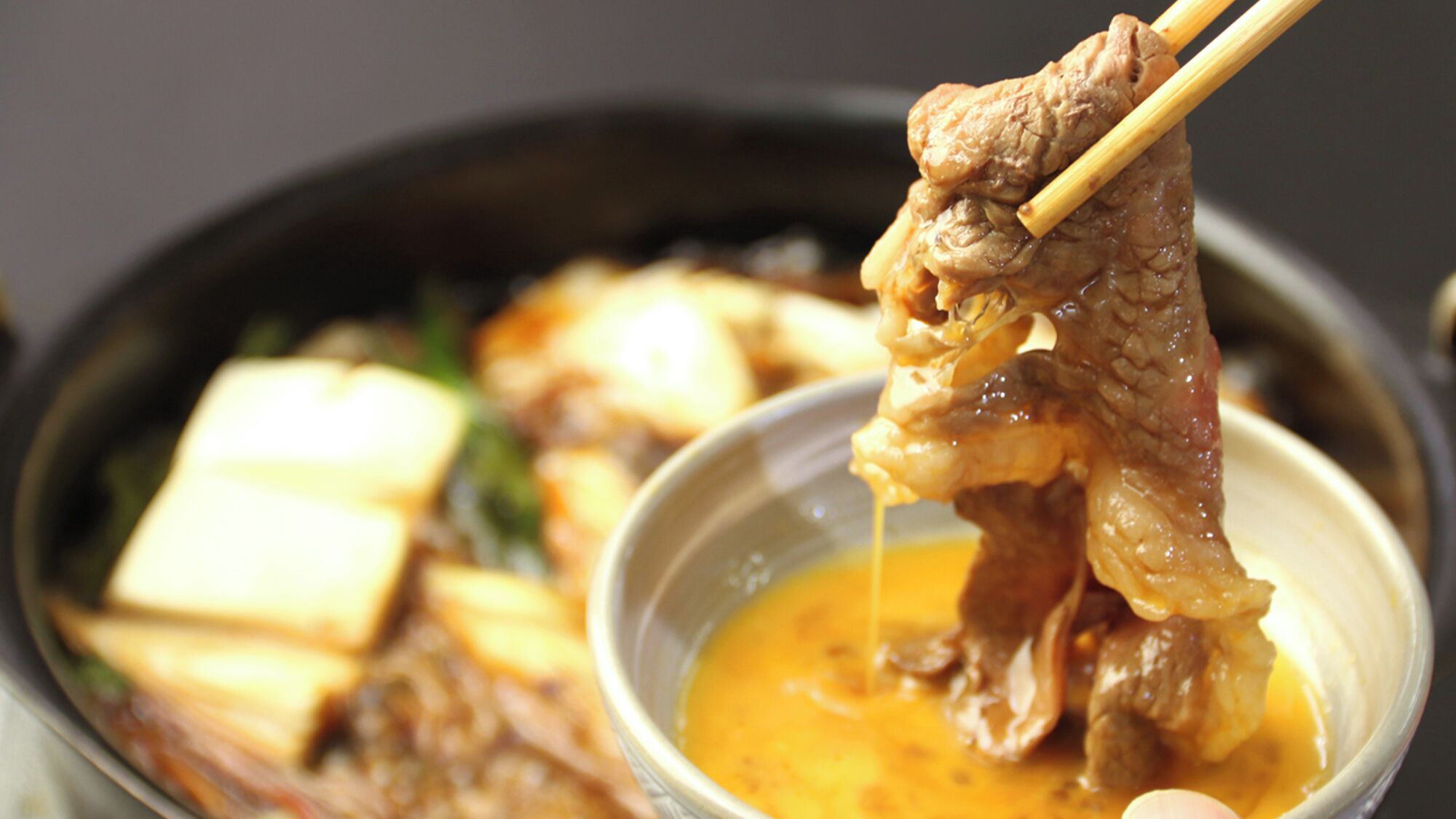 Un bol de sopa amb carn i tofu, agafat amb baquetons.