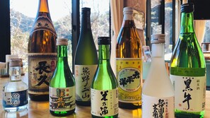 A variety of sake bottles on a wooden table with a view of trees through a window. - Tsurunoyu Onsen (Minabe)