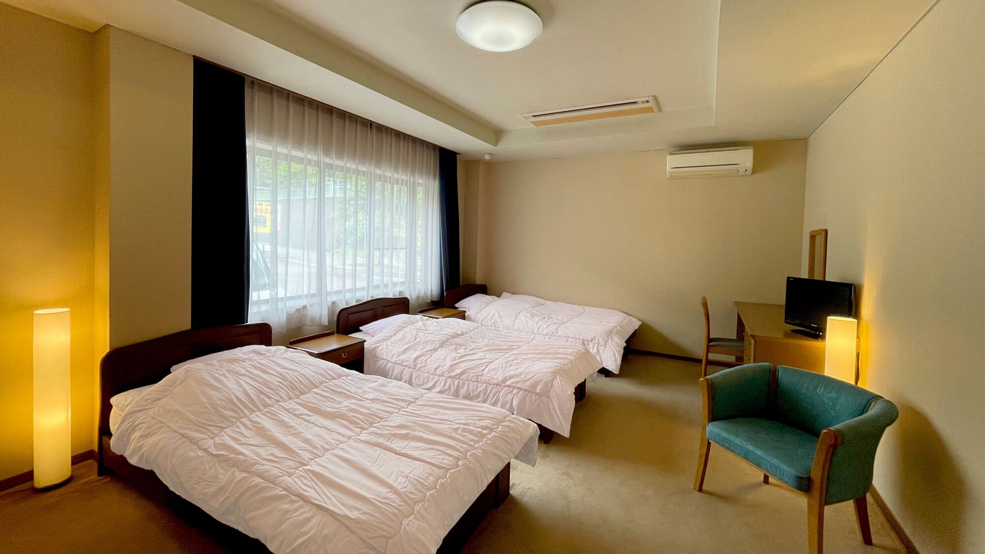 A hotel room with two beds, a TV, a chair, and a window with curtains.