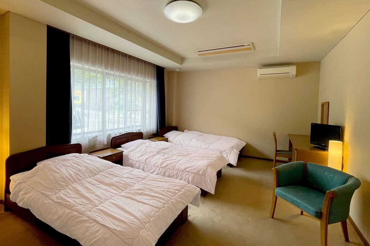 Une chambre d’hôtel avec deux lits, une télévision, une chaise et une fenêtre avec des rideaux.
